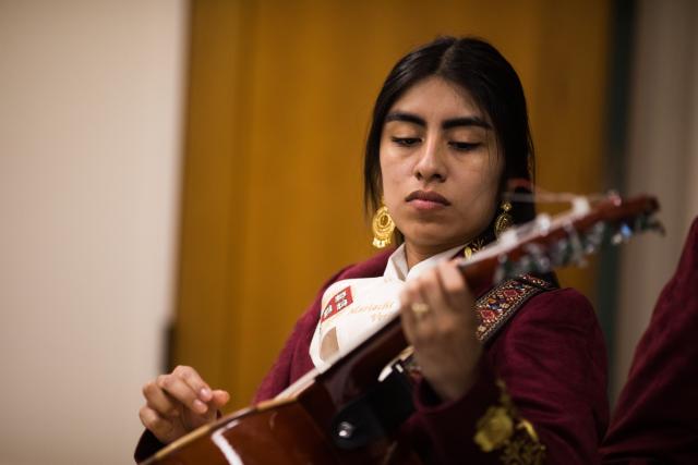 A female mariachi musician holds her instrument while wearing her mariachi suit